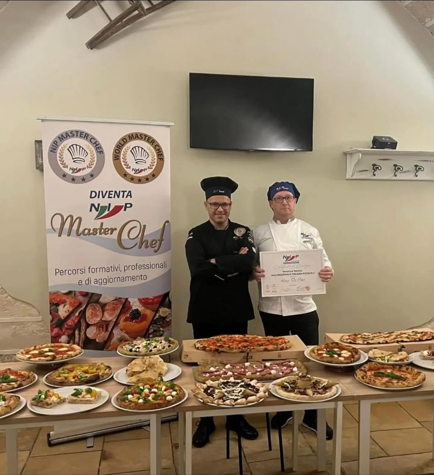 Luigi De Cicco riceve il certificato di istruttore tecnico della Nazionale Italiana Pizzaioli (NIP) davanti a un tavolo di pizze